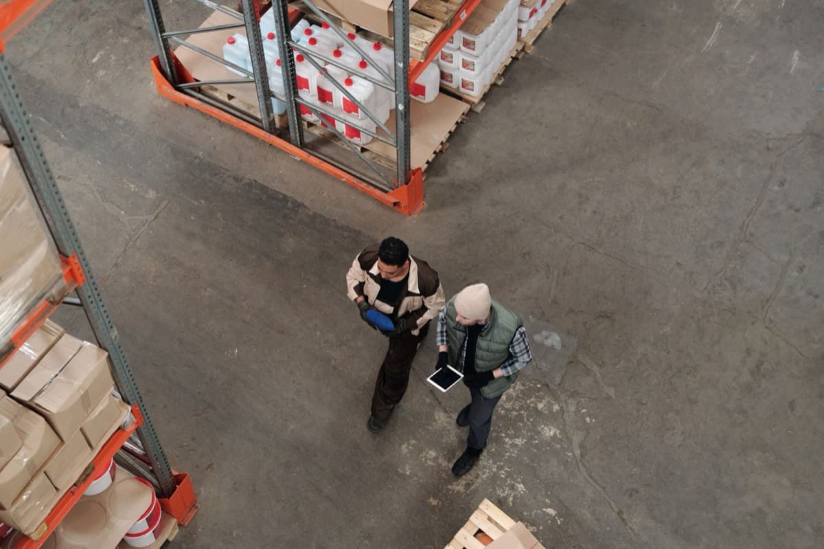 Two warehouse staff reviewing inventory on a tablet between storage racks
