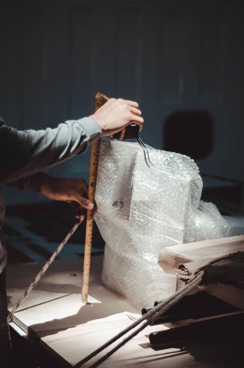 Hands measuring a bubble-wrapped package with a ruler before shipping